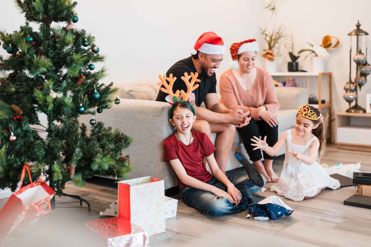 Children excitedly unwrapping Christmas presents at home while their parents sit nearby, capturing festive joy, family bonding, and holiday warmth, happy family moment at weekend.