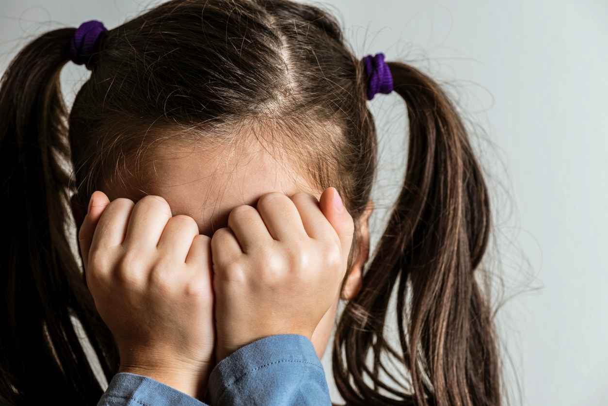 Little crying girl with double ponytail who is hiding her face with her hands. Representing child abuse and domestic violence.